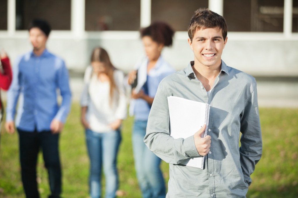 Man Holding Books With Students In Background On Campus